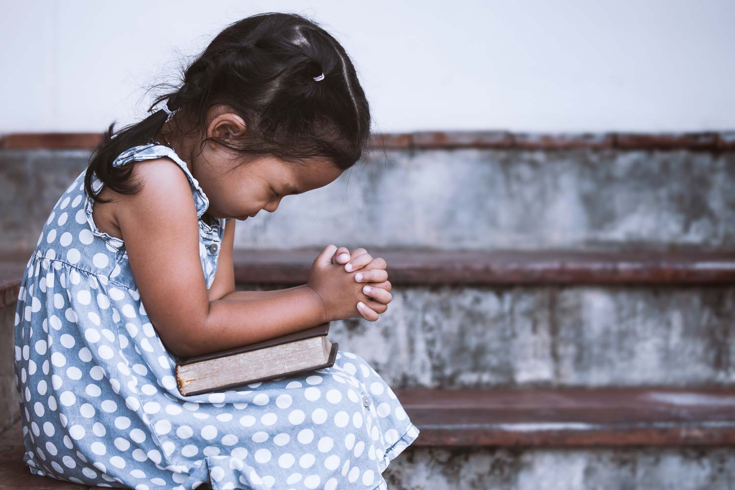 girl prays over a Bible in her lap